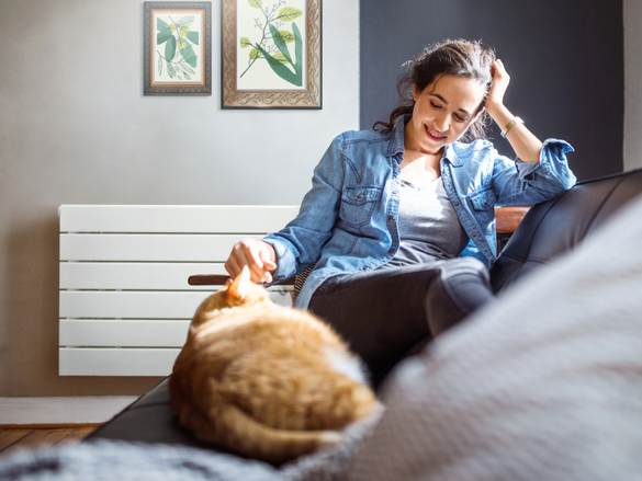 Beautiful young woman relaxing on sofa with her cat in living room.